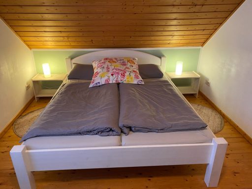 Doppelbett mit grauer Bettwäsche und dekorativem Kissen in einem gemütlichen Schlafzimmer.