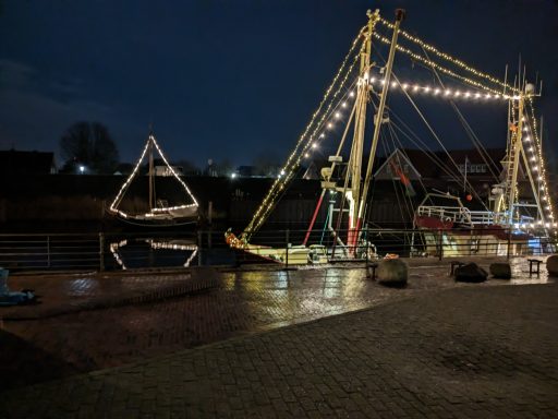 Beleuchteter Hafen mit Schiff und beleuchtetem Boot auf dem Wasser bei Nacht.