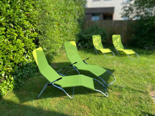 Vier grüne Liegestühle stehen auf einer Rasenfläche in einem Garten.