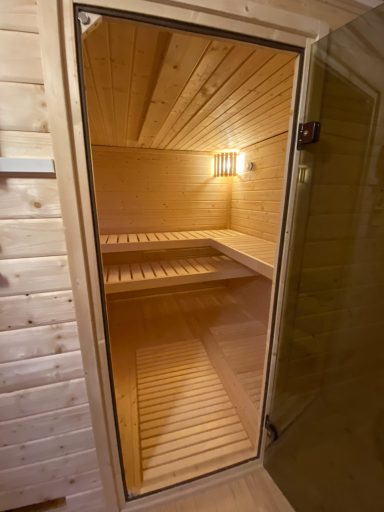 Holzsauna mit geöffneter Tür und schlichten, hell beleuchteten Innenraum.