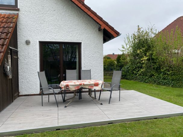 Terrasse mit Tisch und Stühlen, umgeben von Gras und Bäumen.