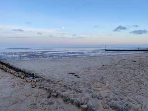 Strandlandschaft mit Wasser und sanften Wellen unter einem blauen Himmel.