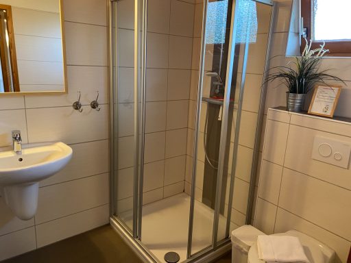 Badezimmer mit Dusche, Waschbecken, Spiegel und Handtüchern.