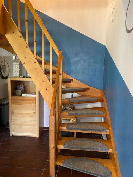 Holztreppe mit blauer Wand, gepolsterten Stufen und einem Sichtbereich zur Raumgestaltung.