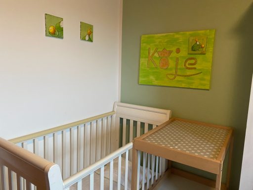 Ein helles Kinderzimmer mit einem Bettchen und einem Wickeltisch an einer grünen Wand.