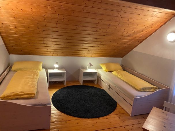 Gemütliches Dachzimmer mit zwei Betten, Nachttischen und Teppichboden.
