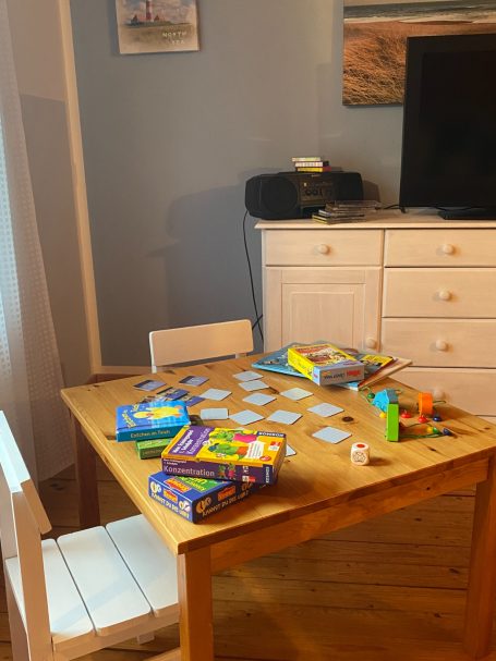 Holztisch mit Spielen, Karten und Spielzeug, umgeben von einem Stuhl und Möbeln.