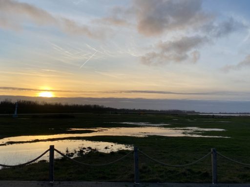 Sonnenuntergang über einem ruhigen Gewässer mit grasbewachsenem Ufer.