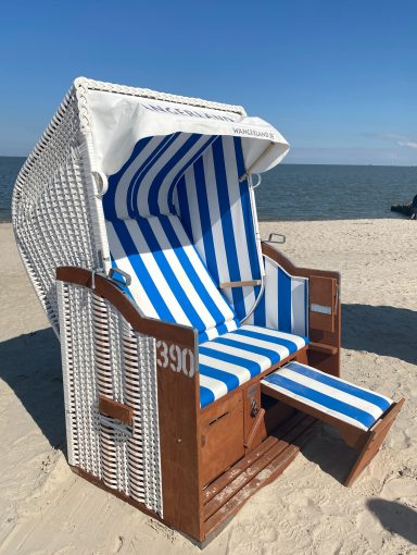 Strandkorb mit blau-weißem Streifenmuster am Strand vor dem Meer.