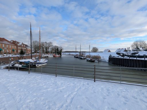 Winterliche Hafenansicht mit Booten und Schnee, unter bewölkten Himmel.